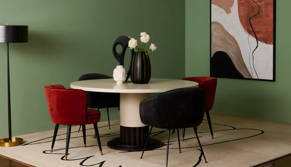 A dining room set with green walls, a round table, four chairs, an artwork and a floor lamp.