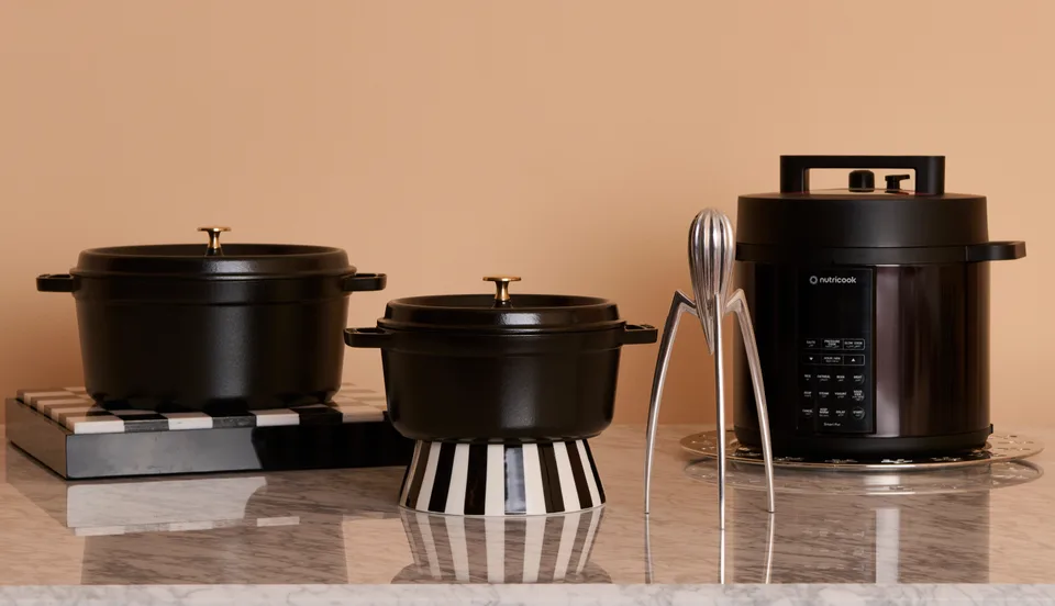 Black cookware and a countertop appliance arranged on stone-effect surfaces against a peach wall.