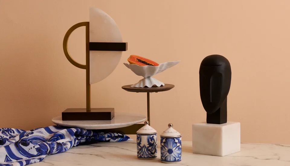 Sculptural objects and patterned tableware arranged at different heights against a peach wall.