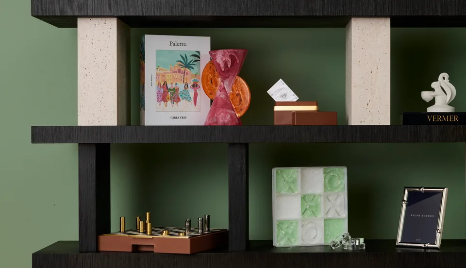 Books and decorative objects displayed on dark open shelves against a green wall.