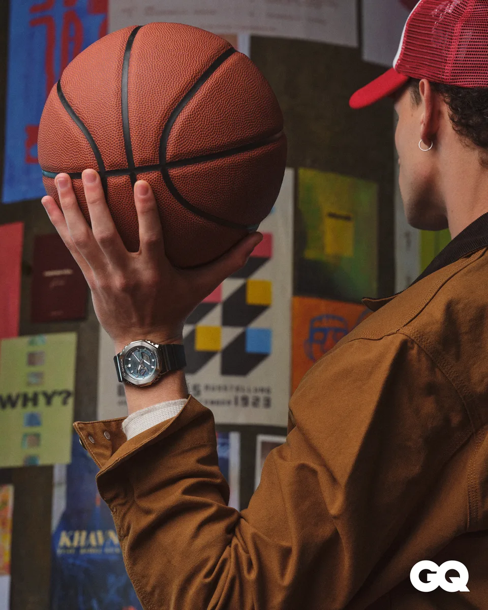 A model holding a basketball wears a Casio watch against a wall of graphic posters.