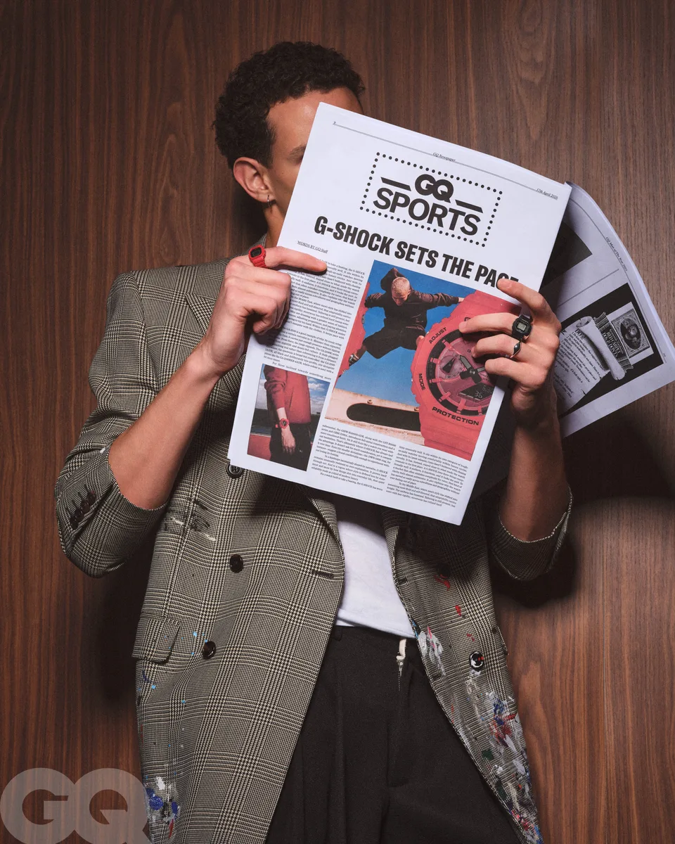 A model reads a GQ sports newspaper in front of wood panelling, with a Casio watch visible.