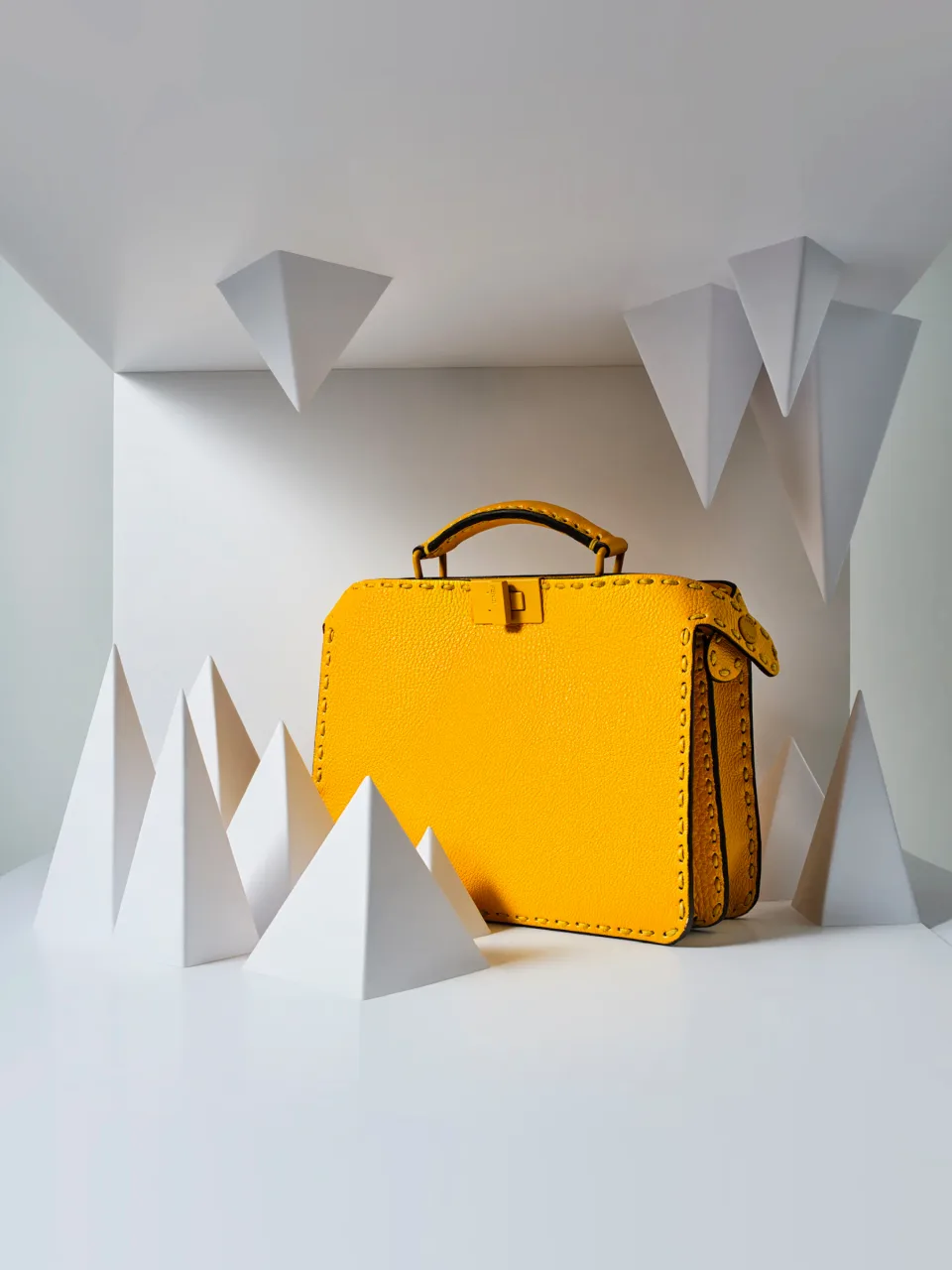 Yellow handbag among white geometric paper forms