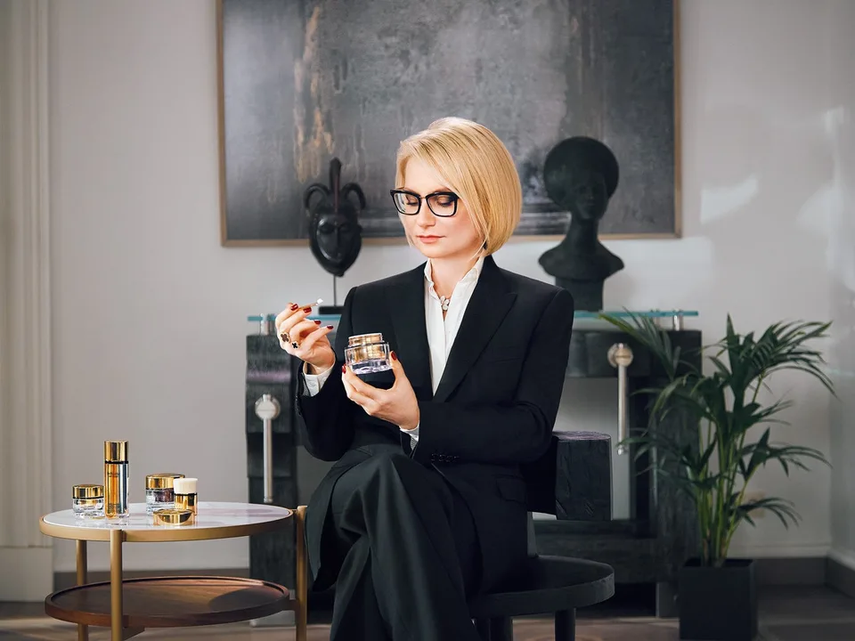 A person holds an Estée Lauder jar beside a small table of skincare products.