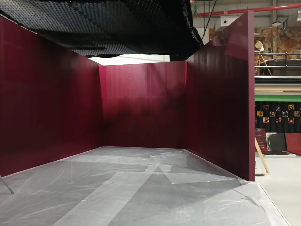 Freestanding red walls form a room inside the studio, with the surrounding workspace visible beyond them.