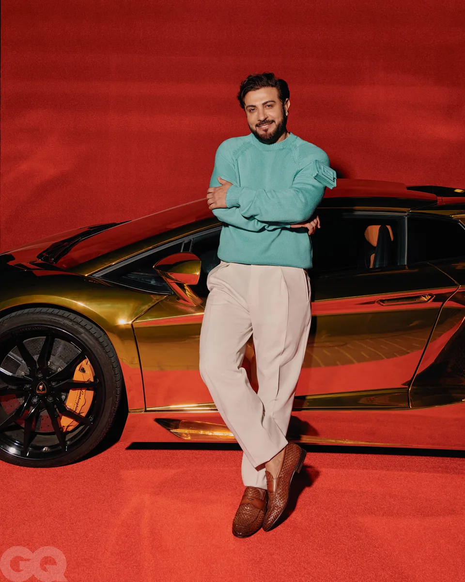 A portrait beside a metallic car on the red floor and backdrop.