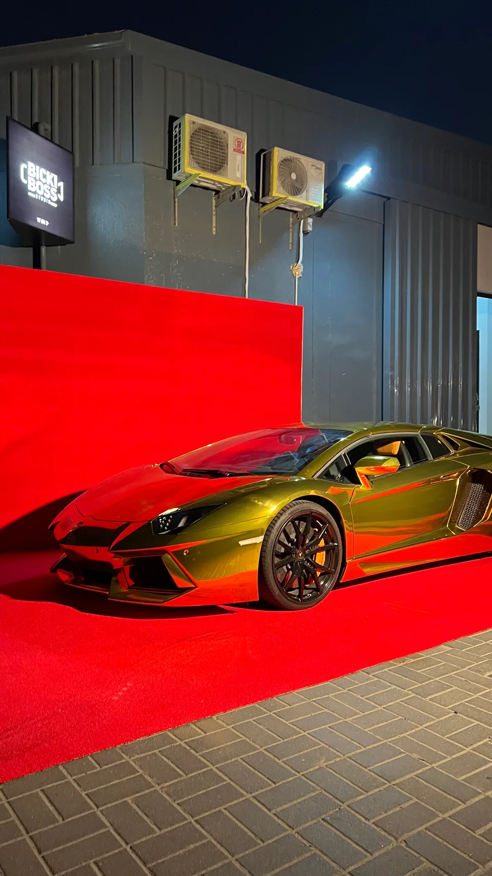 The red floor and backdrop are installed around a metallic car outside the studio.
