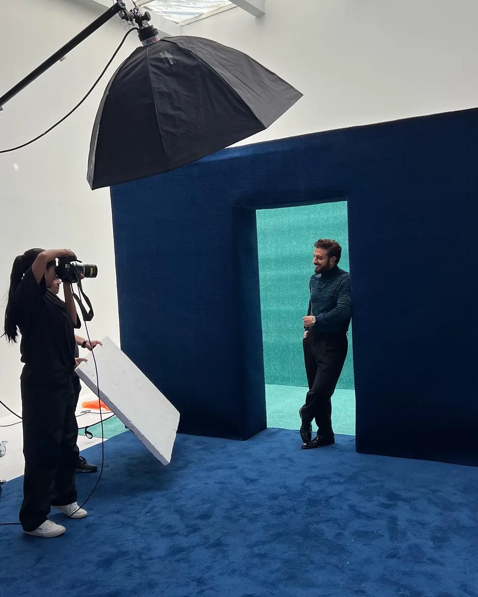 The photographer works in front of a blue doorway and green backdrop in the studio.