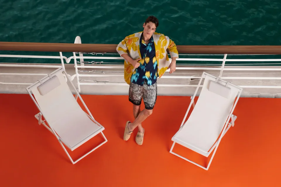 Person standing on an orange deck beside white lounge chairs and water