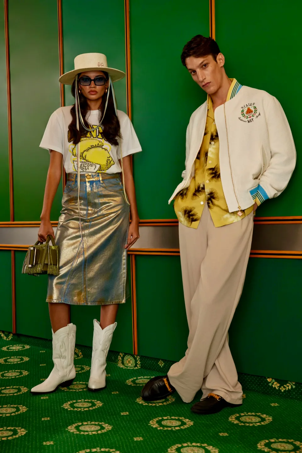 Two people wearing colourful outfits in front of a green panelled wall
