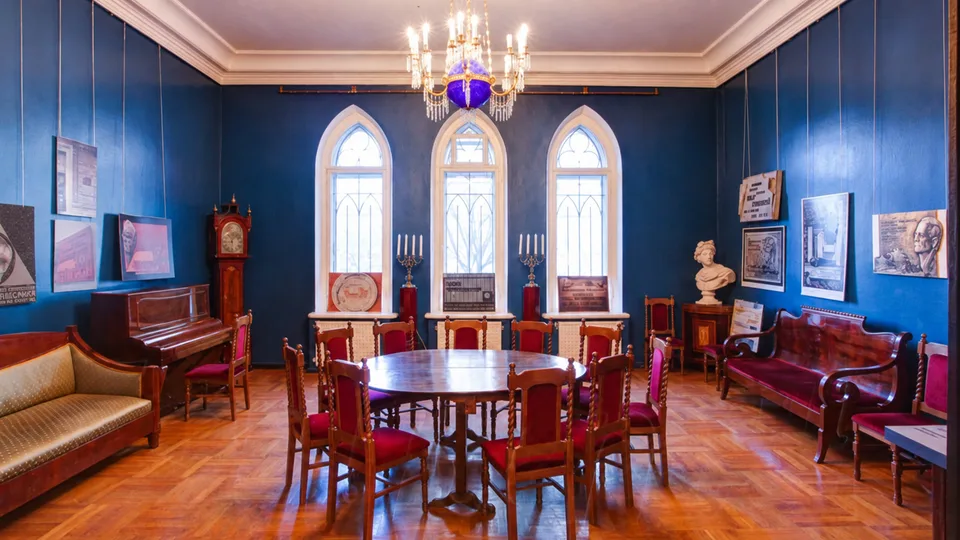 The original blue room with three pointed windows, a chandelier, parquet floor, a table, chairs and sofas.