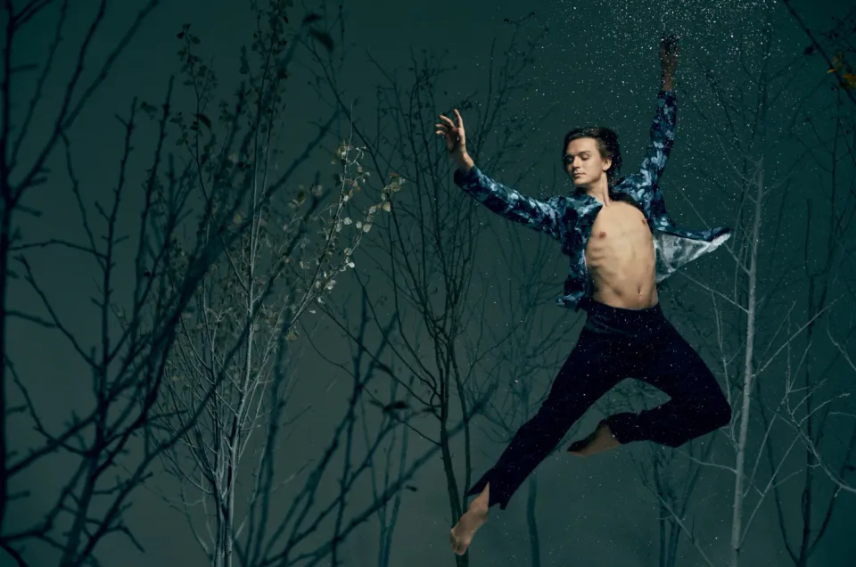 Person jumping among bare trees against a dark teal backdrop