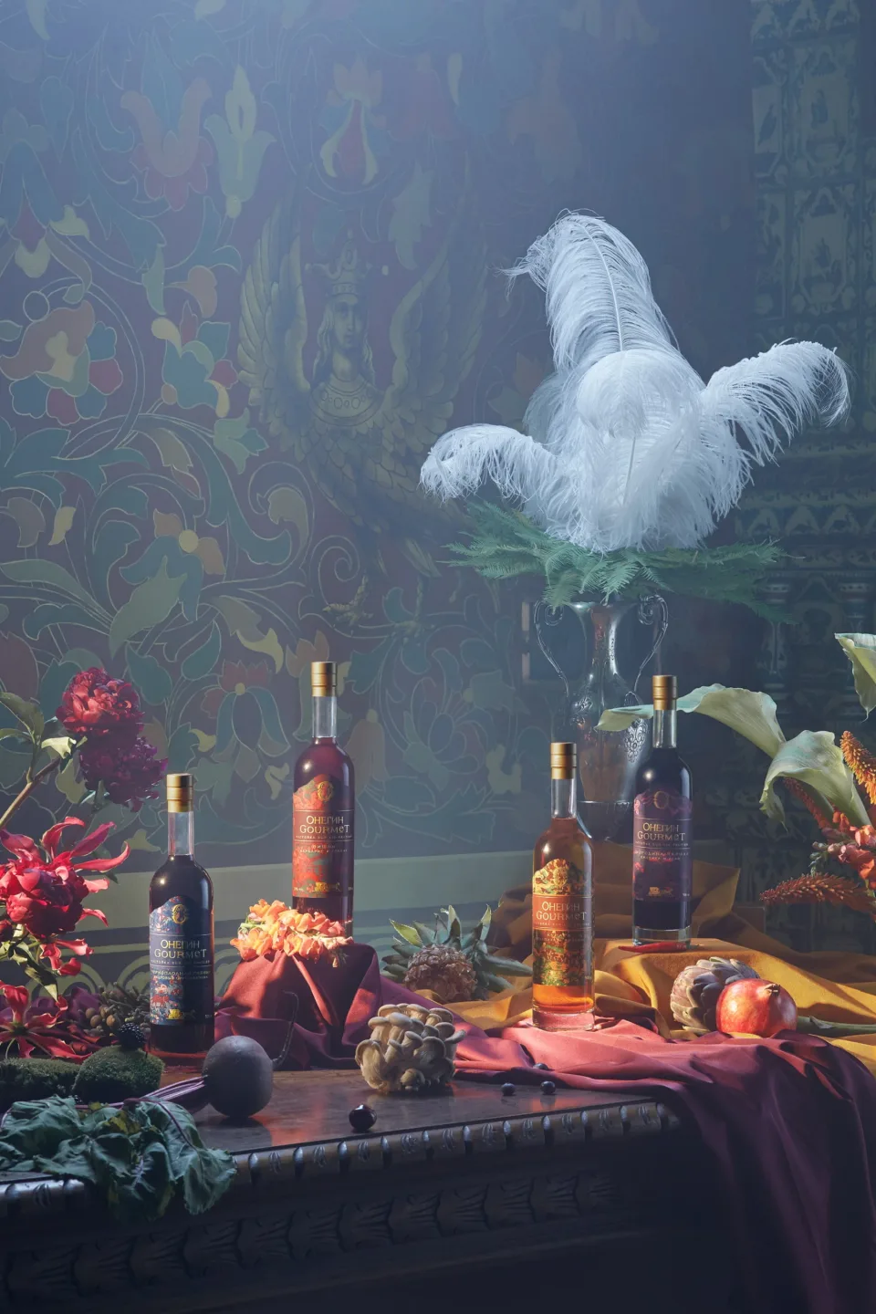 Several Onegin Gourmet bottles arranged on an ornate table beneath a silver vase with white feathers, fruit and flowers.