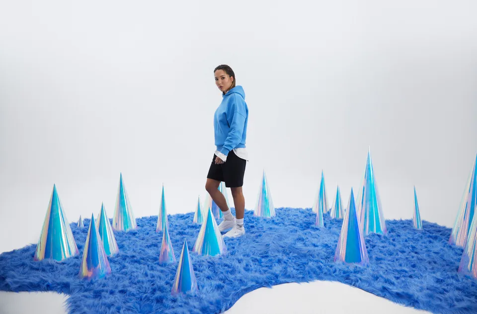 A model stands on blue textured flooring surrounded by reflective cone-shaped props.