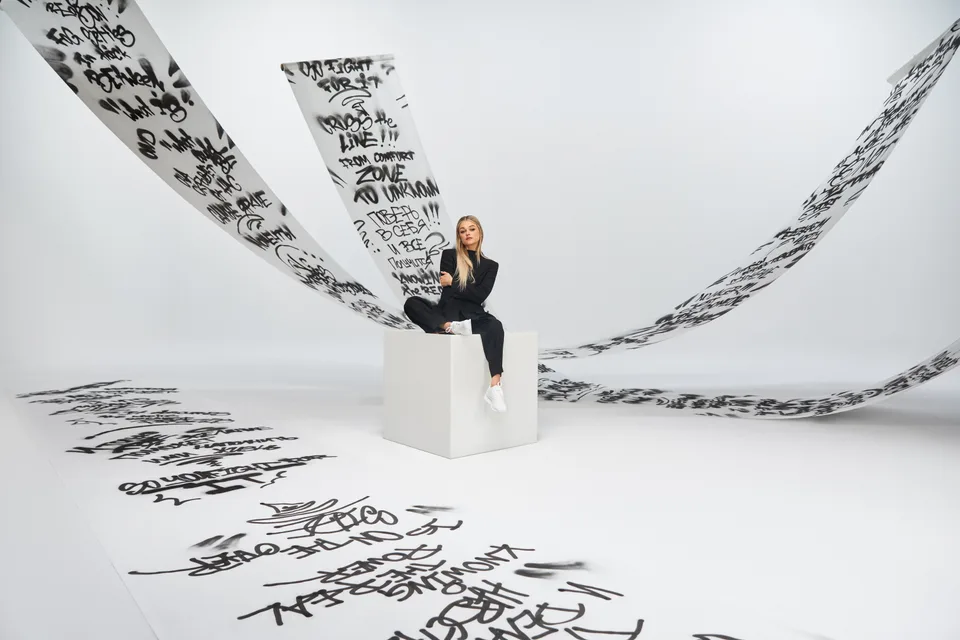 A model sits on a white plinth between sweeping white surfaces covered in black handwritten lettering.