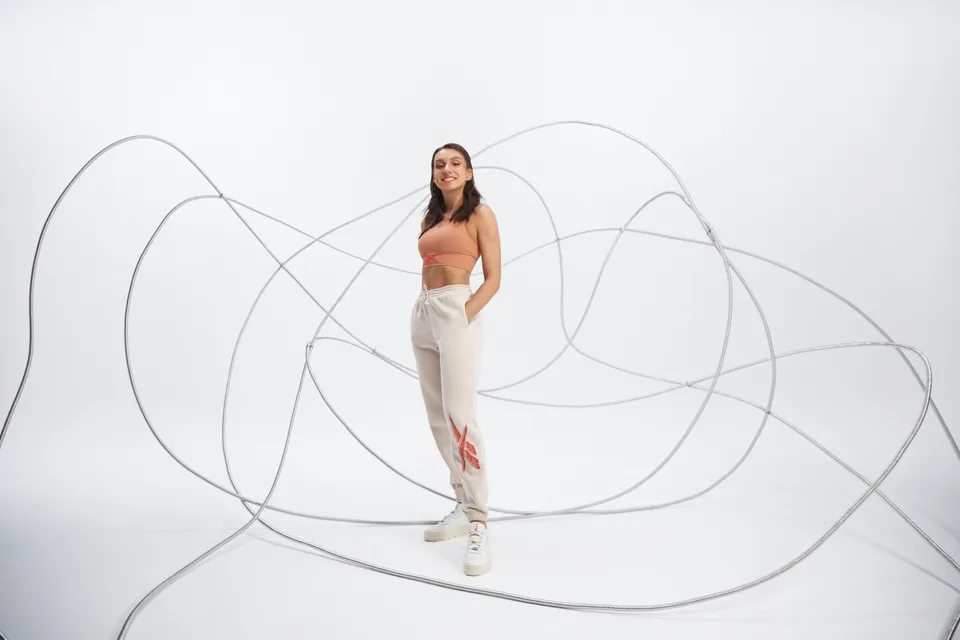 A model stands within a large looping line sculpture in a white studio.