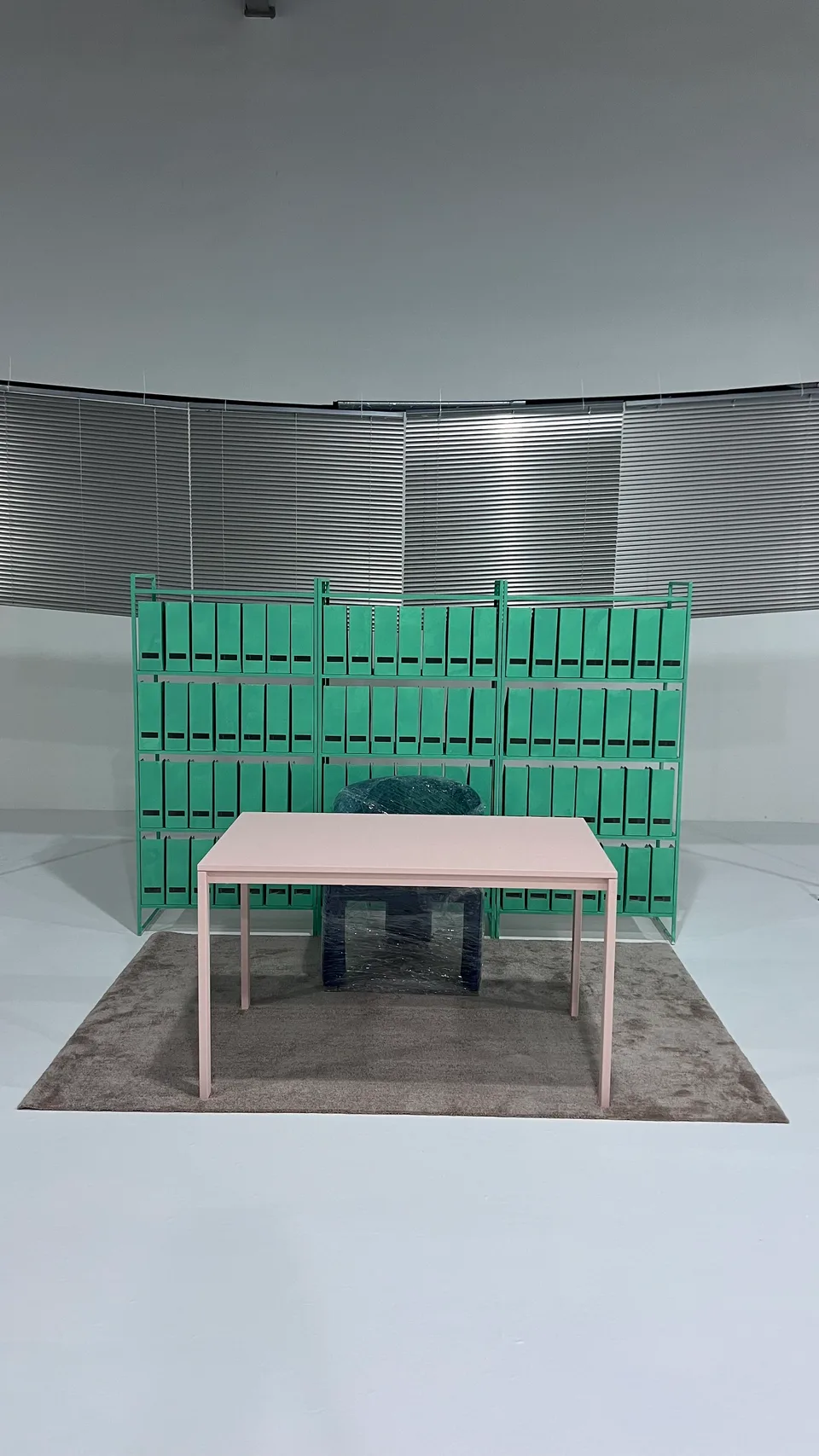 The assembled office set with green folders, a pink desk and a wall of window blinds.