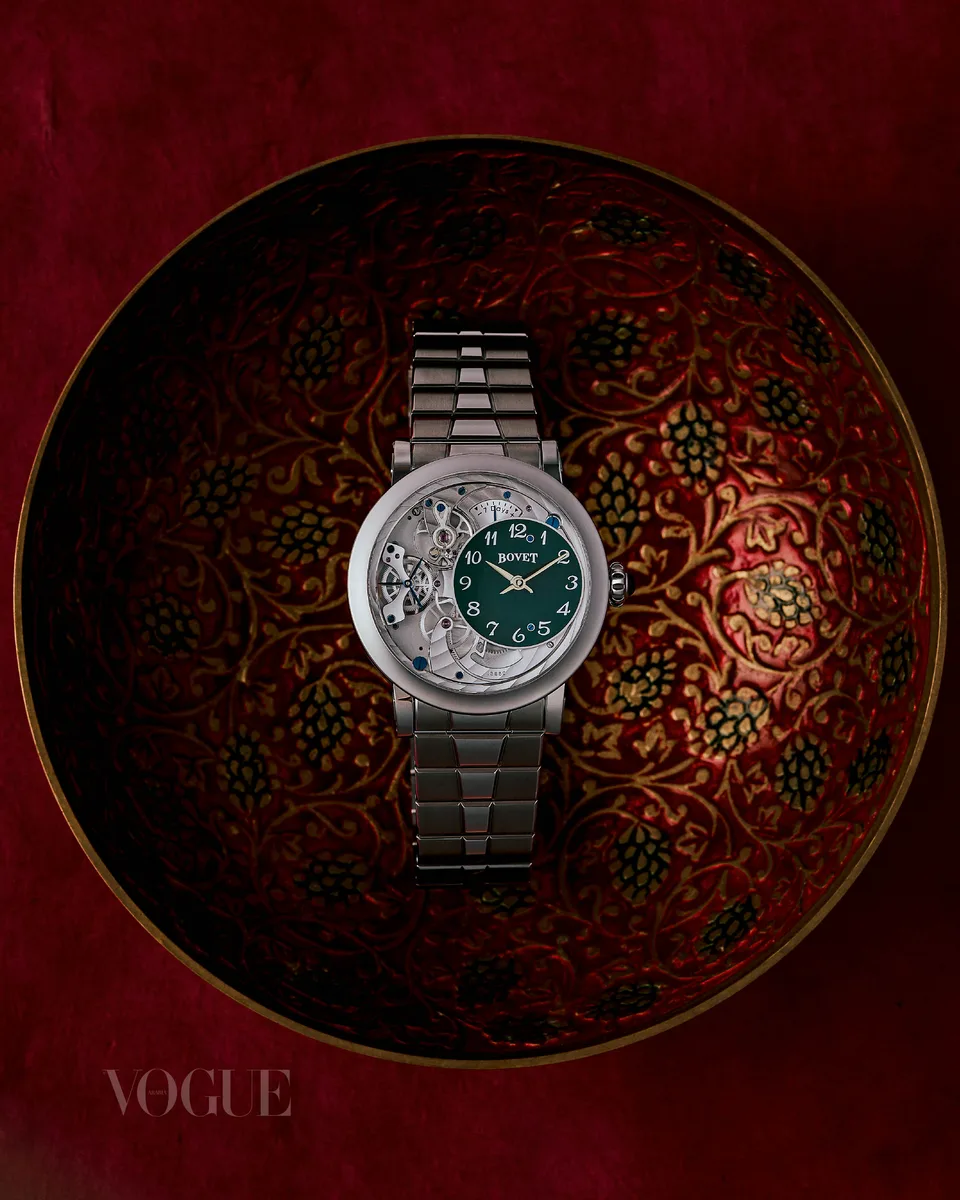 A watch with a green dial rests inside an ornate bowl against deep red fabric.