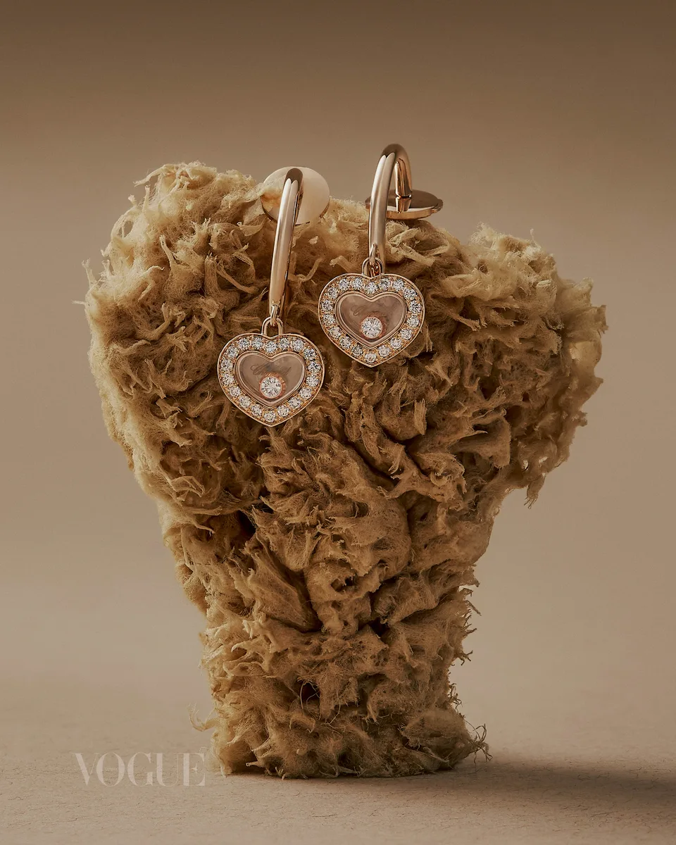 Heart-shaped earrings are displayed on a porous natural form against a soft neutral background.