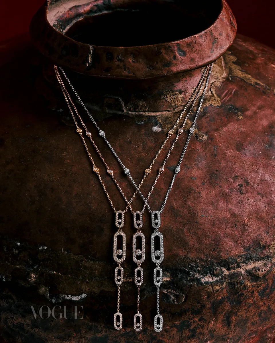 Fine necklaces hang against a large textured vessel.