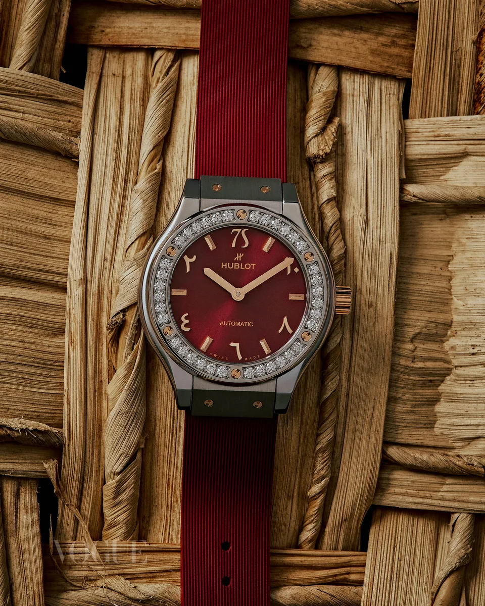 A red-dial watch is arranged against a coarse woven surface.