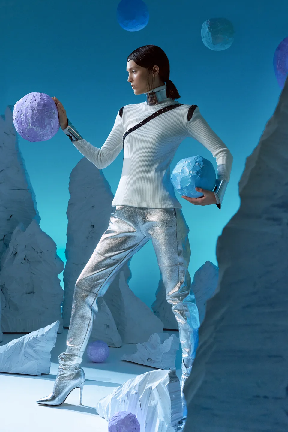 A model holds a textured blue sphere among matching scenic forms.