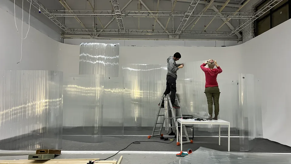 Crew install tall curved translucent panels in a studio using a ladder and platform.