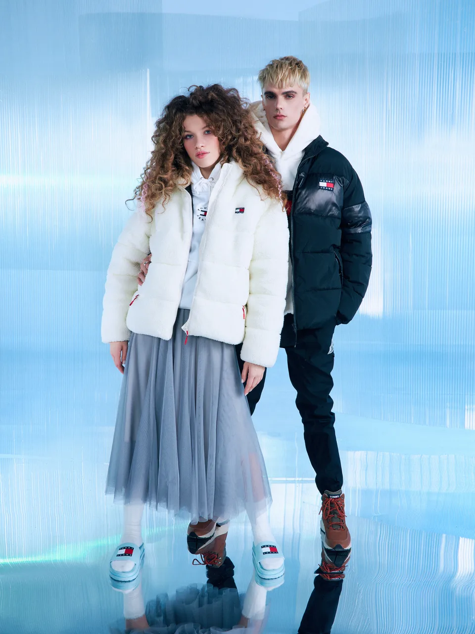 Two models stand between curved translucent surfaces with blue light and floor reflections.